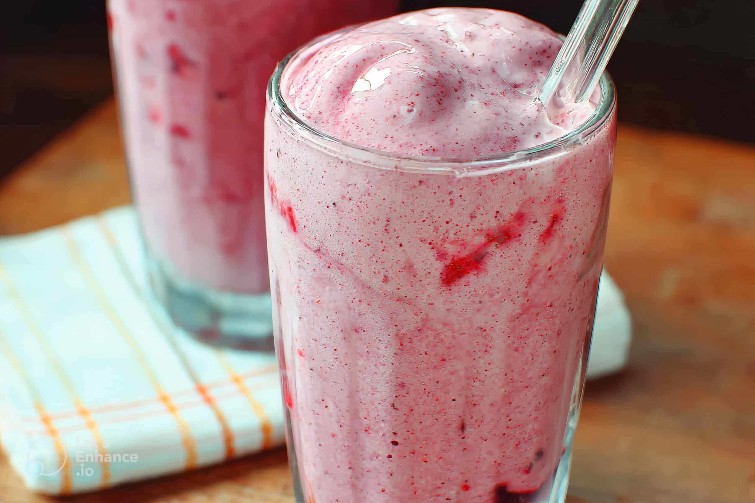 Thick, creamy pink smoothie with swirls of berries served in a glass with a straw